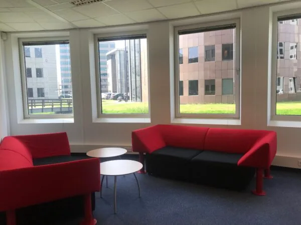Moderne kantoorruimte in Rivium Quadrant met rood-zwarte loungesofa’s en uitzicht op omliggende kantoorgebouwen.